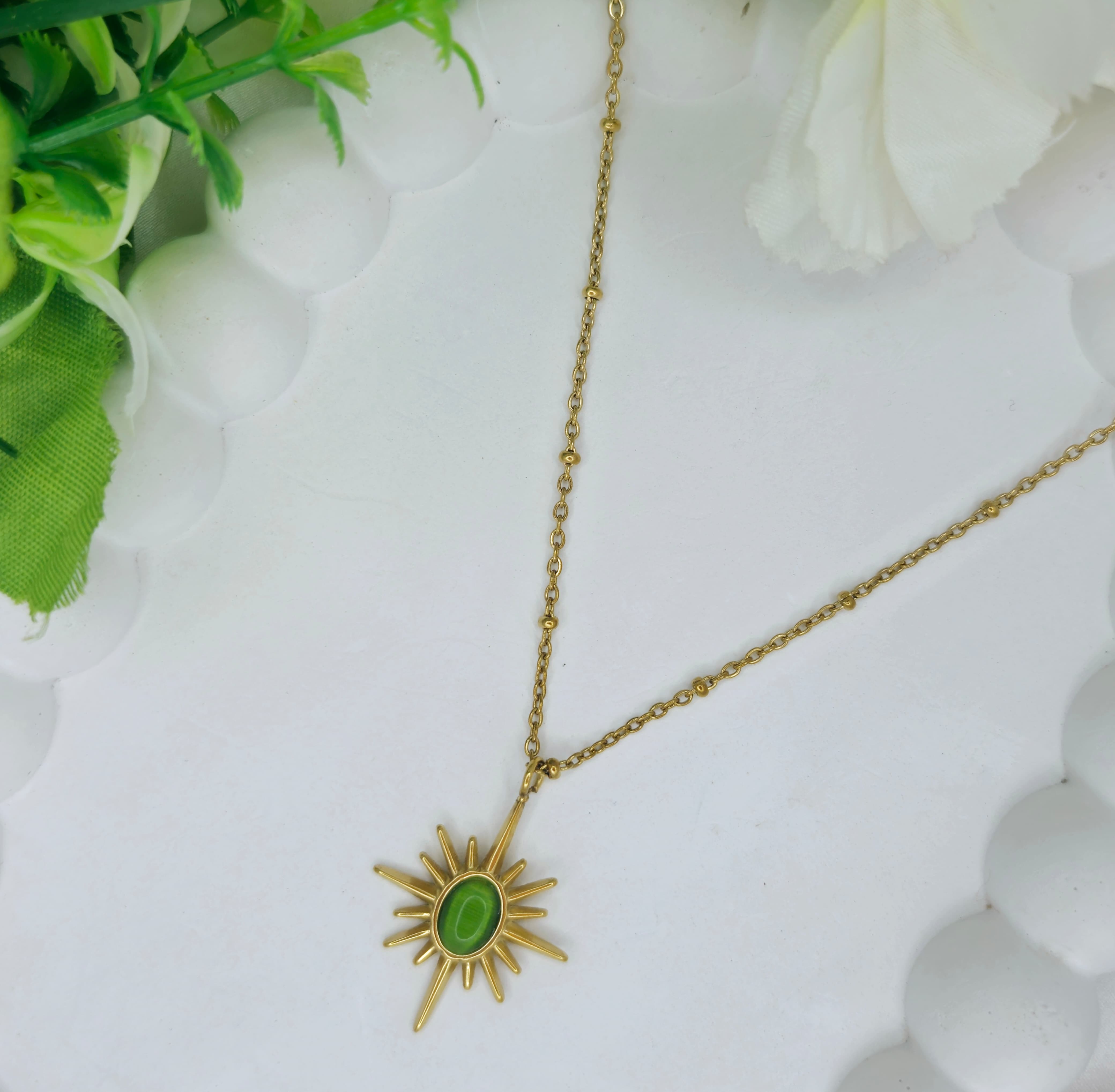Gold necklace with a green pendant on a white background