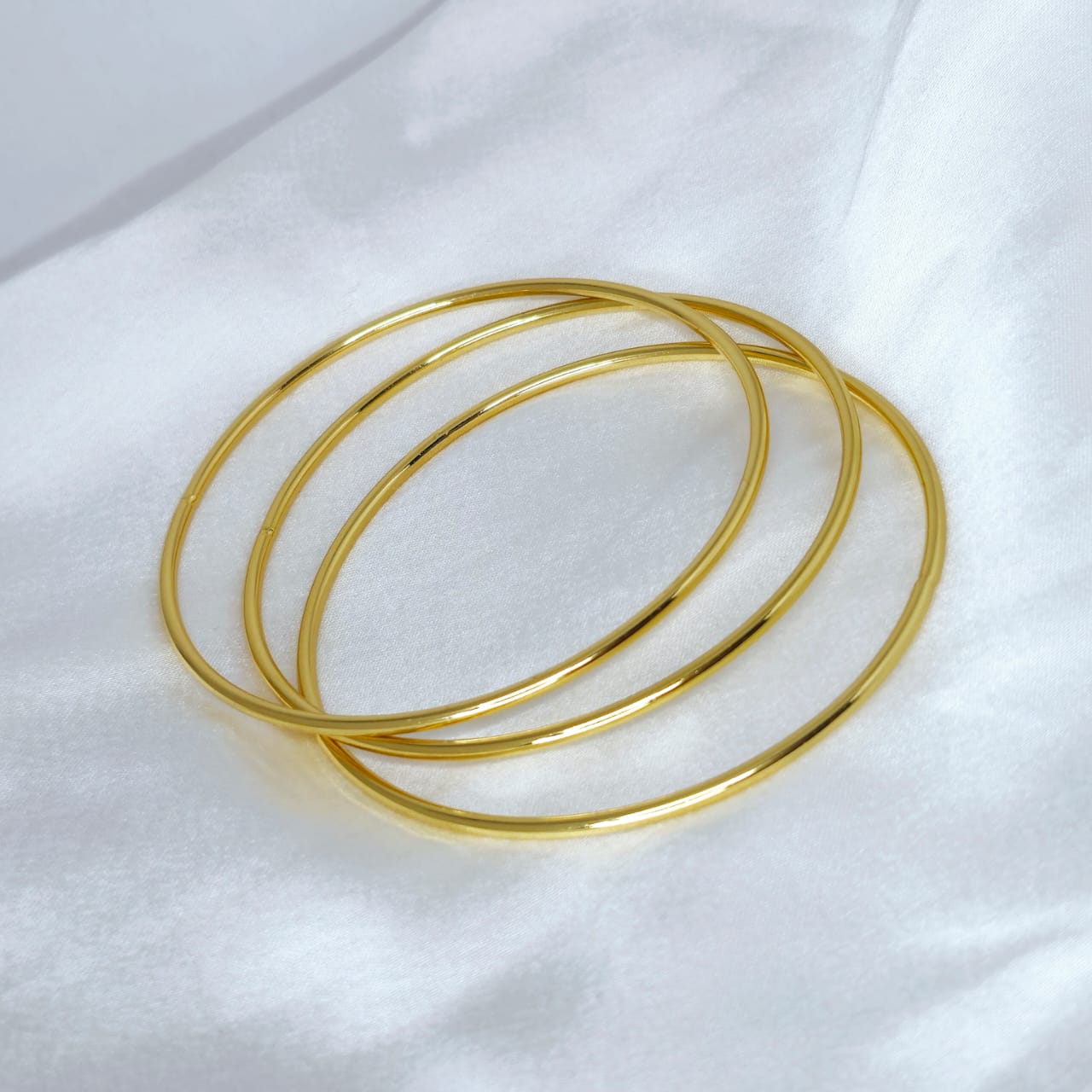 Three gold bangles on a white fabric background