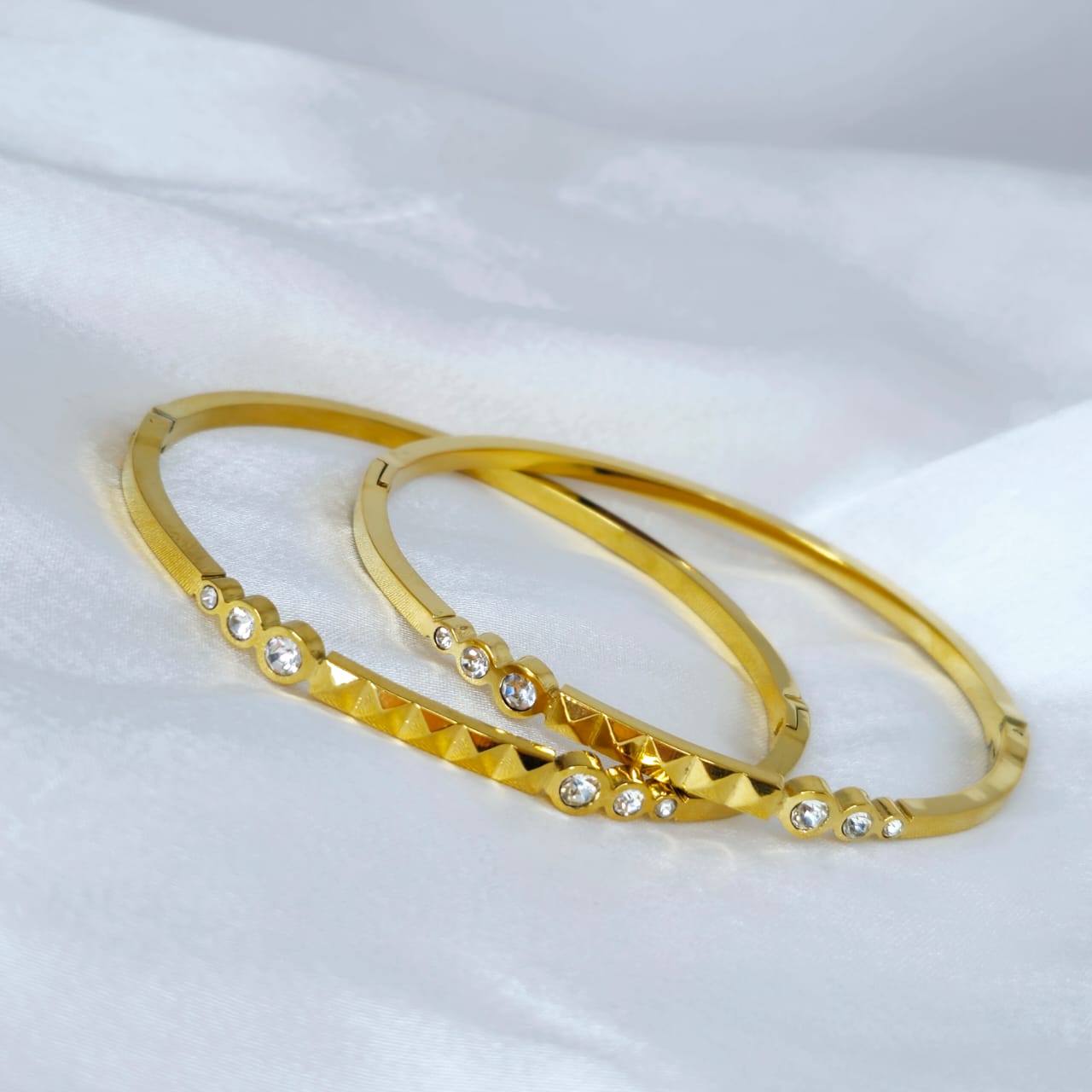 Two gold bangles with diamond-like stones on a white background