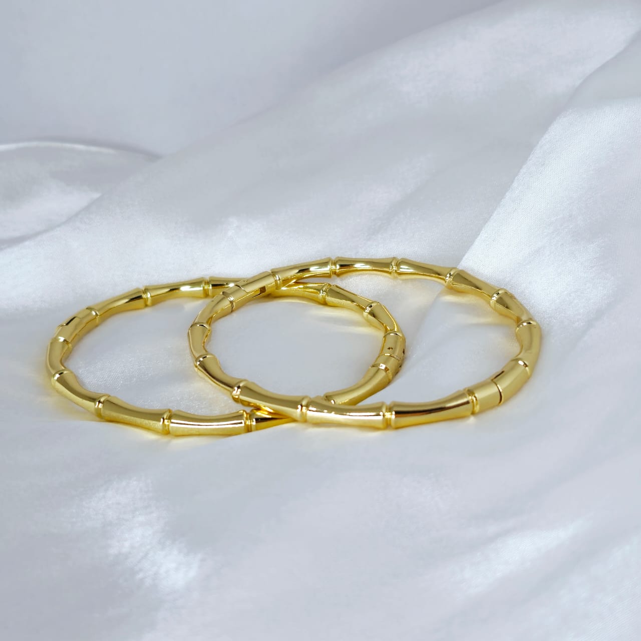 Two gold bangles on a white satin background