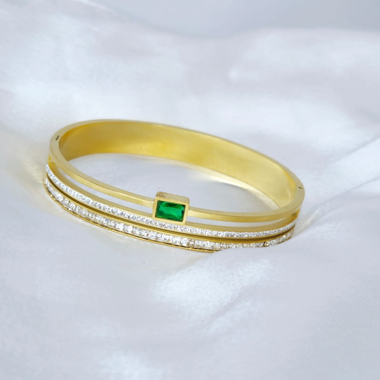 Gold bracelet with a green gemstone on a white background