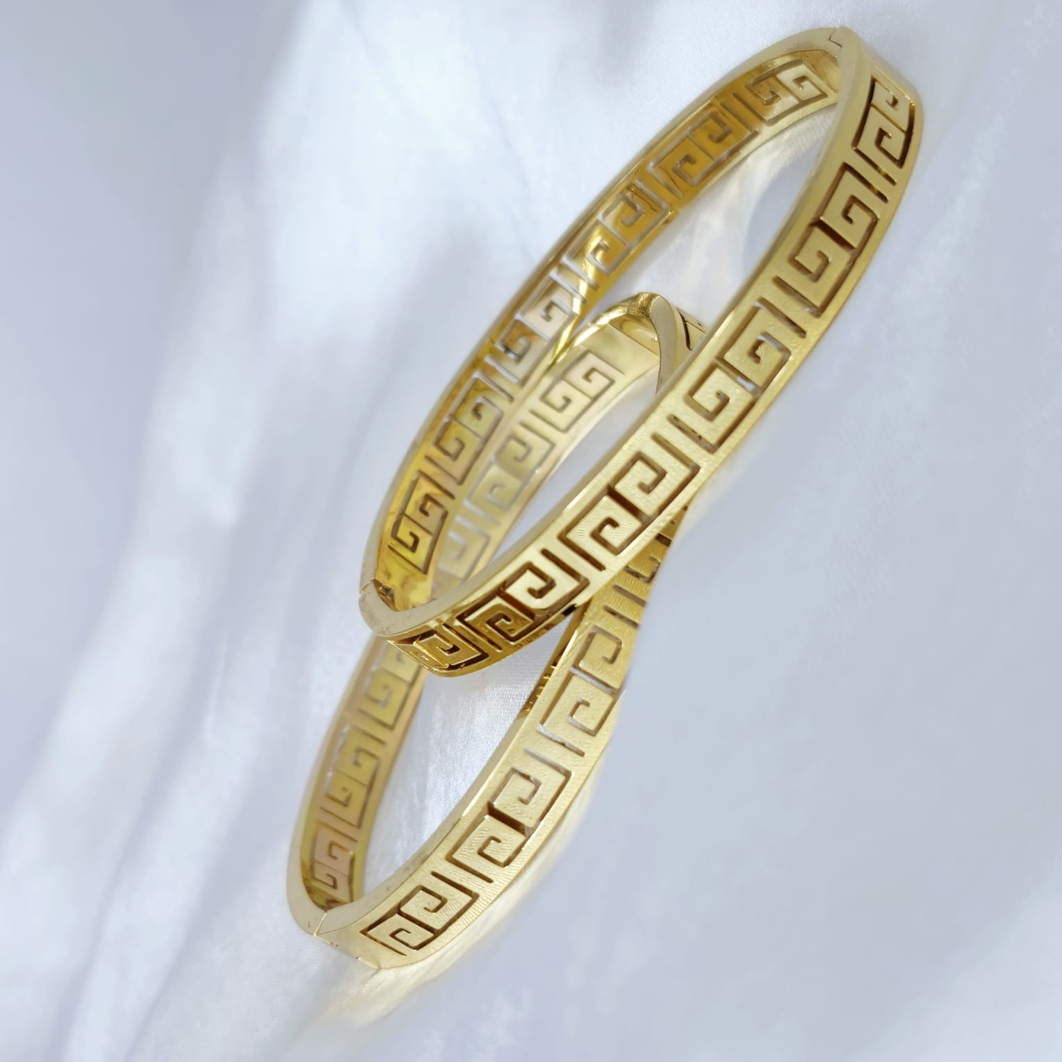 Two gold bangles with intricate patterns on a white background