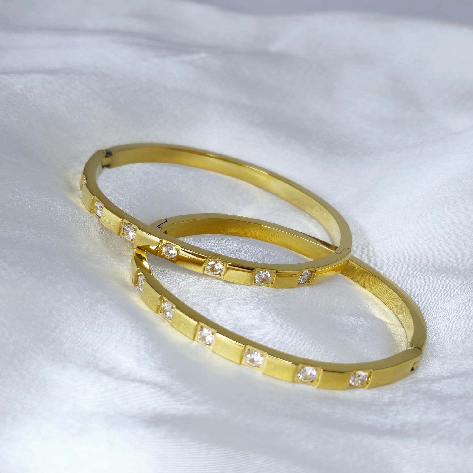 Two gold bangles with embedded stones on a white fabric background