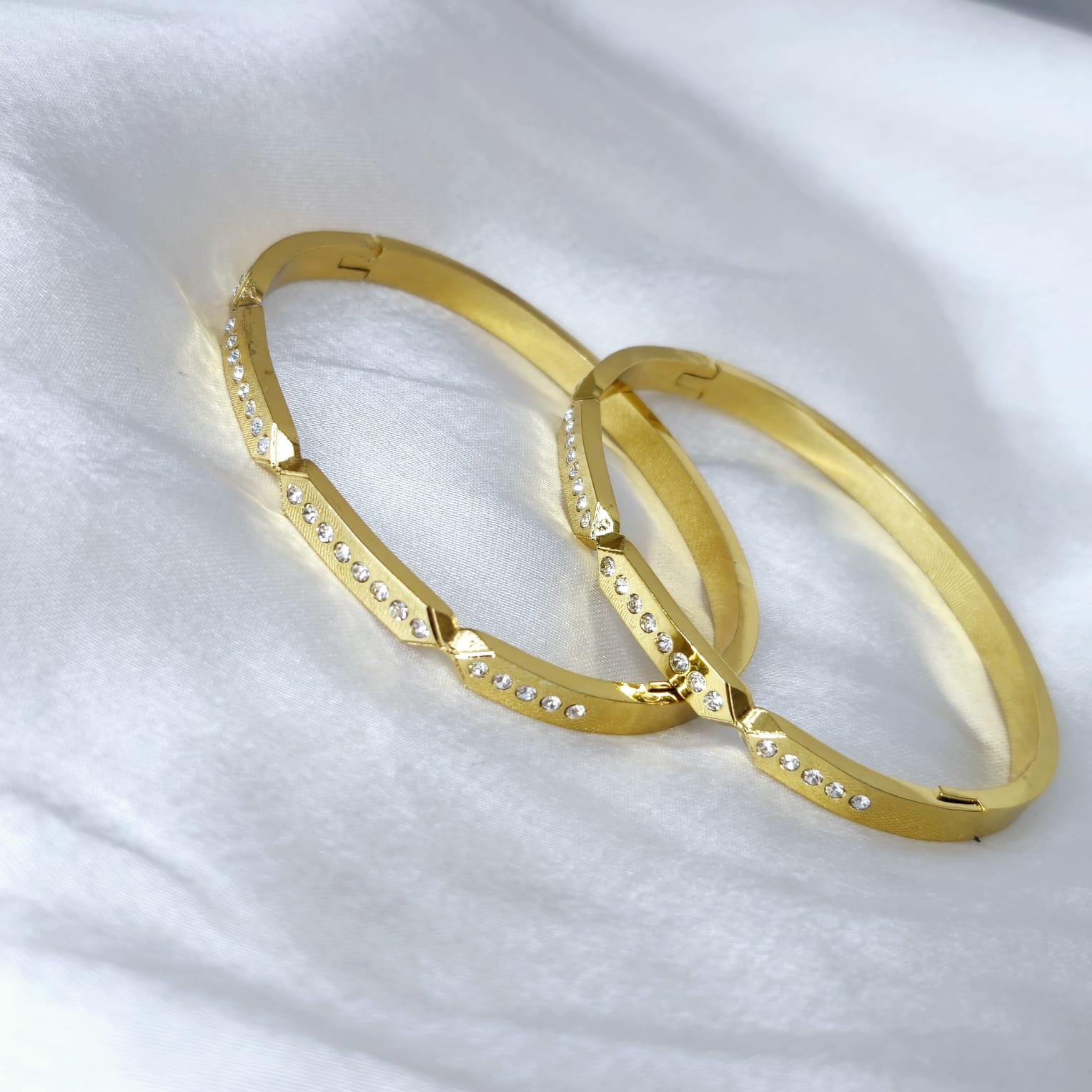 Two gold bangles with diamond accents on a white fabric background