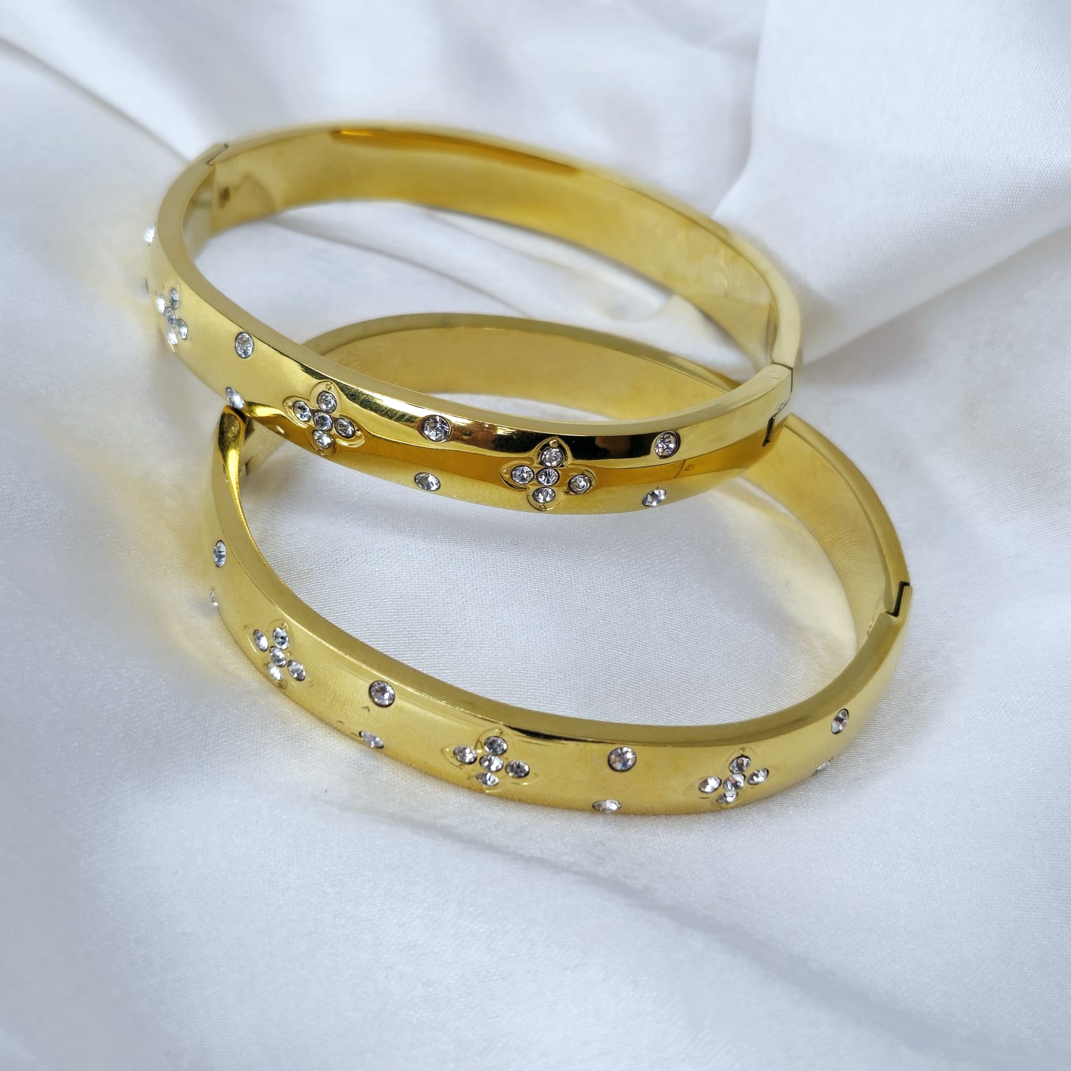 Two gold bangles with small diamonds on a white fabric background