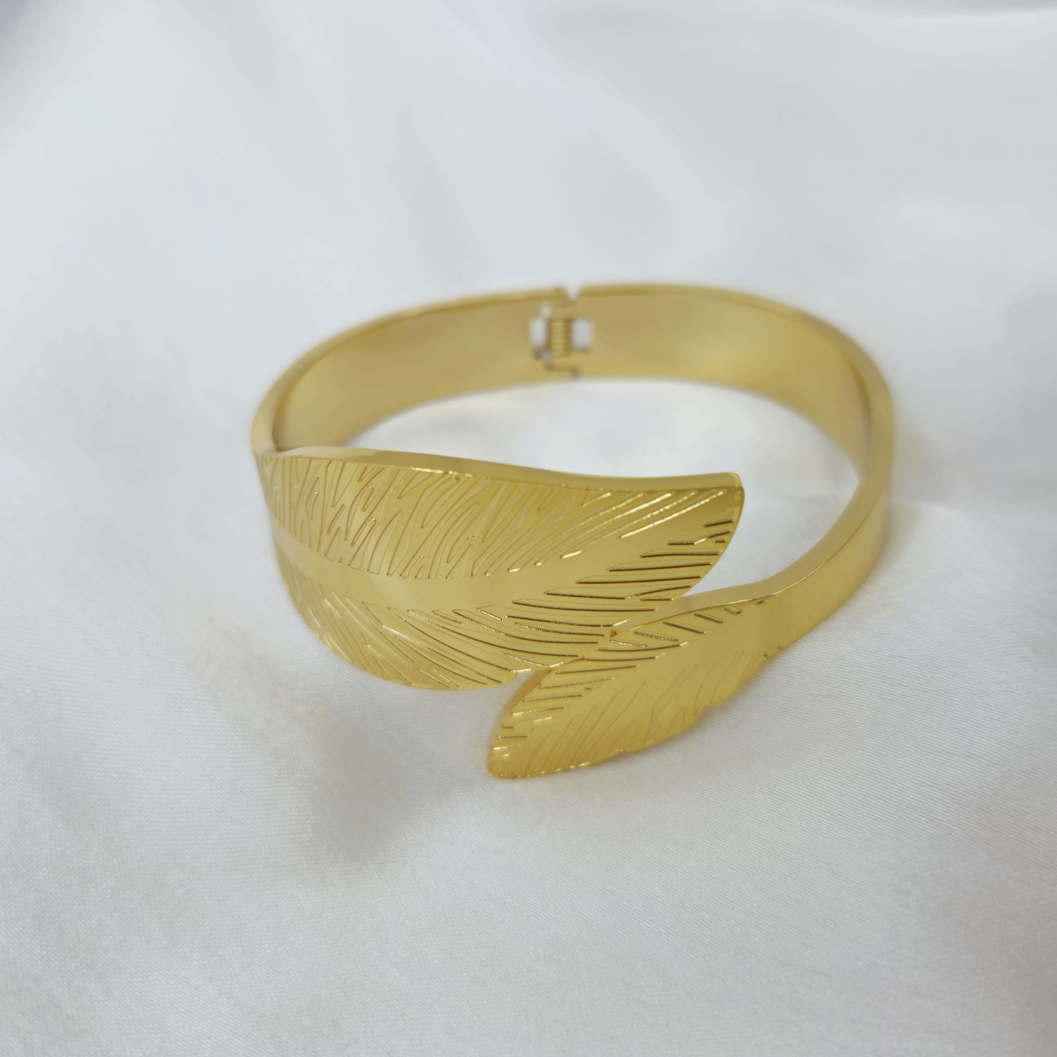 Gold bracelet with feather design on a white background