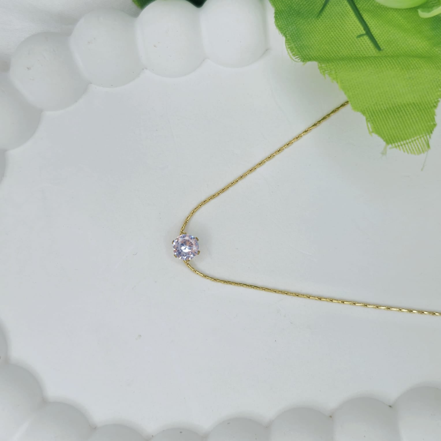 Gold necklace with a pink gemstone on a white surface