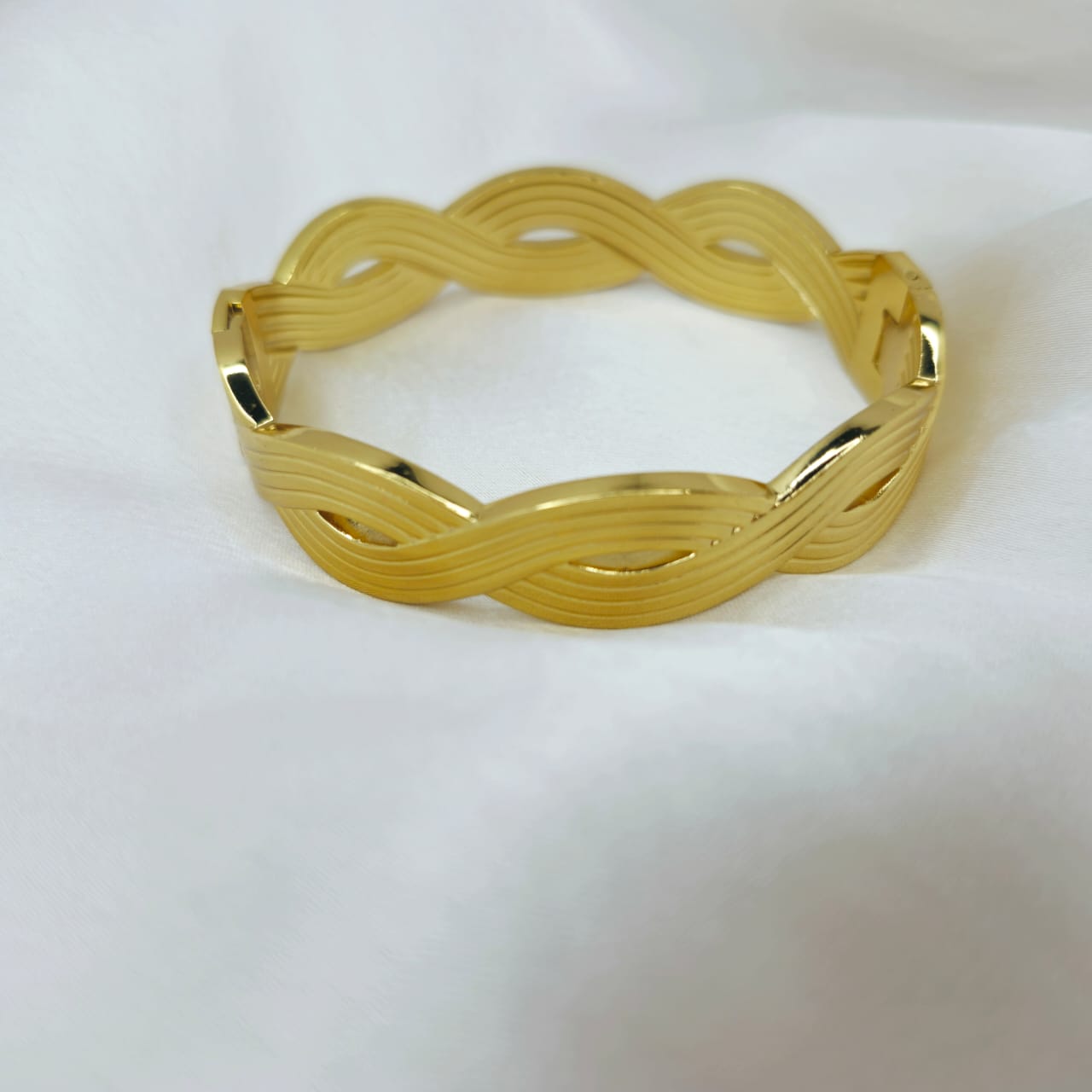 Gold bracelet with wavy design on a white background