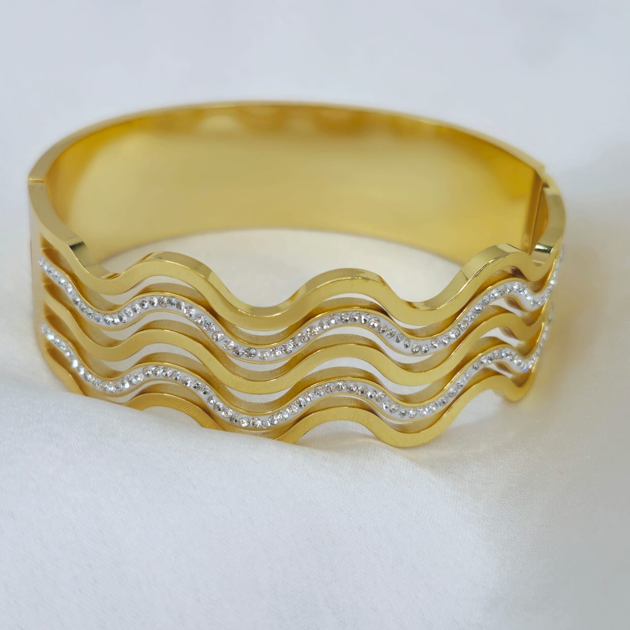 Gold bracelet with wavy design and embedded stones on a white background