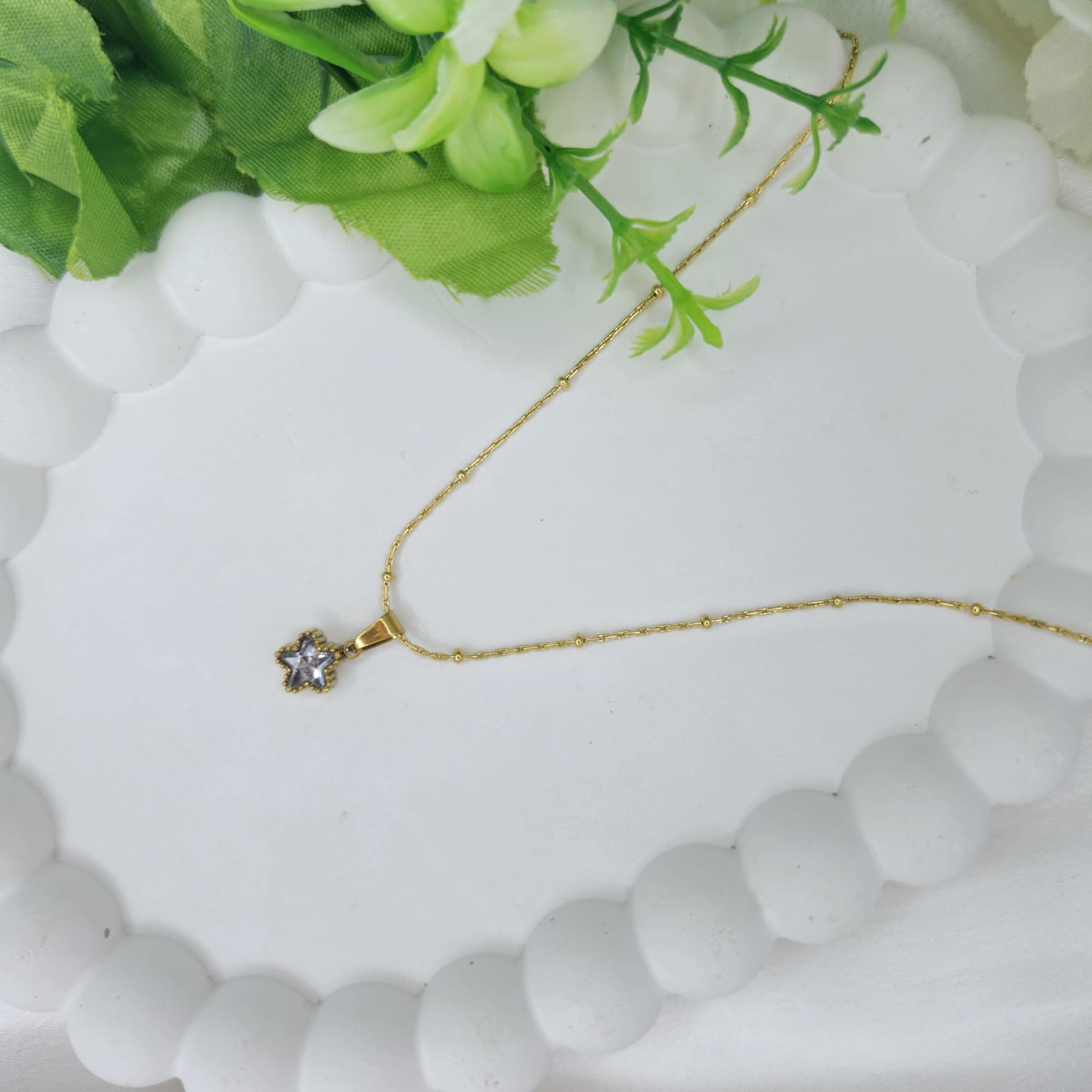 Gold necklace with a star-shaped pendant on a white stone surface with greenery.
