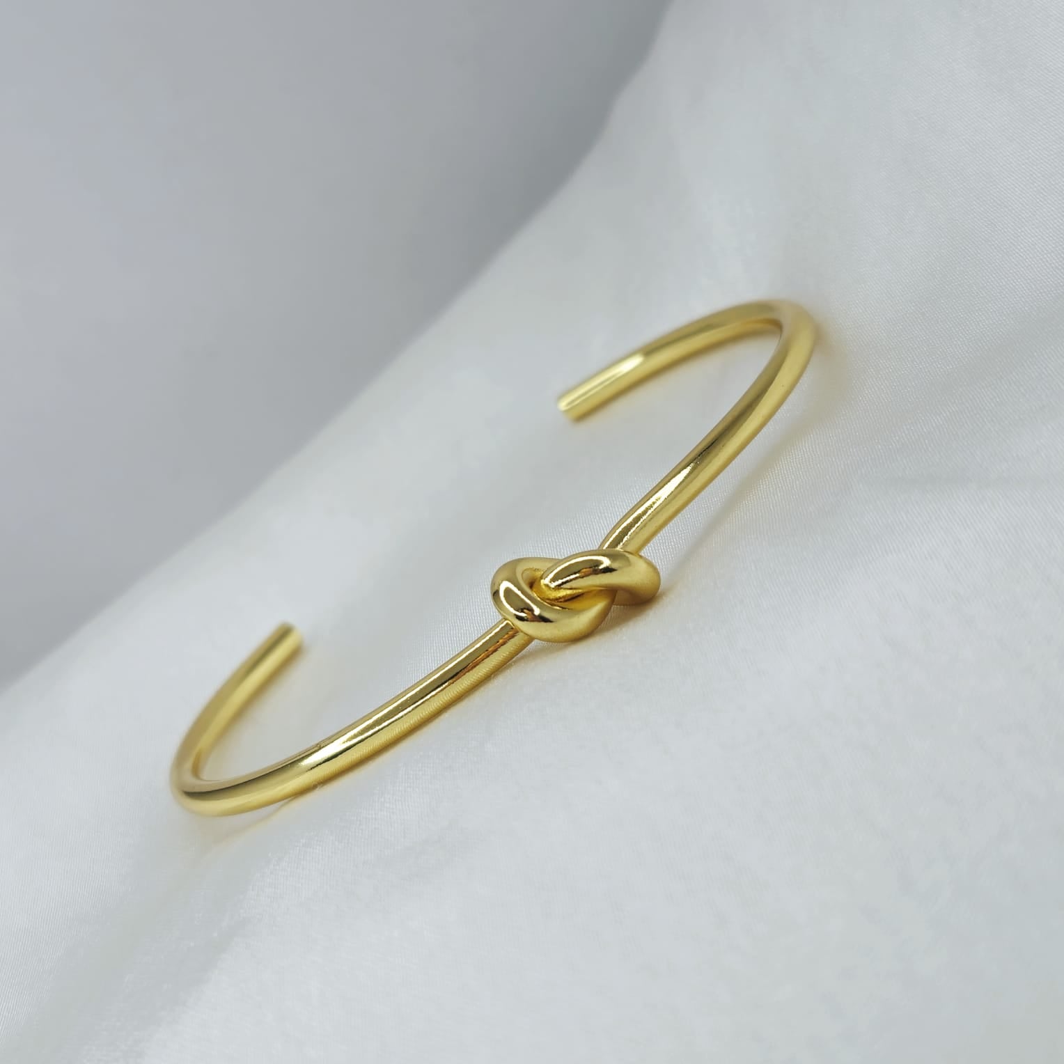 Gold bracelet with a knot design on a white surface