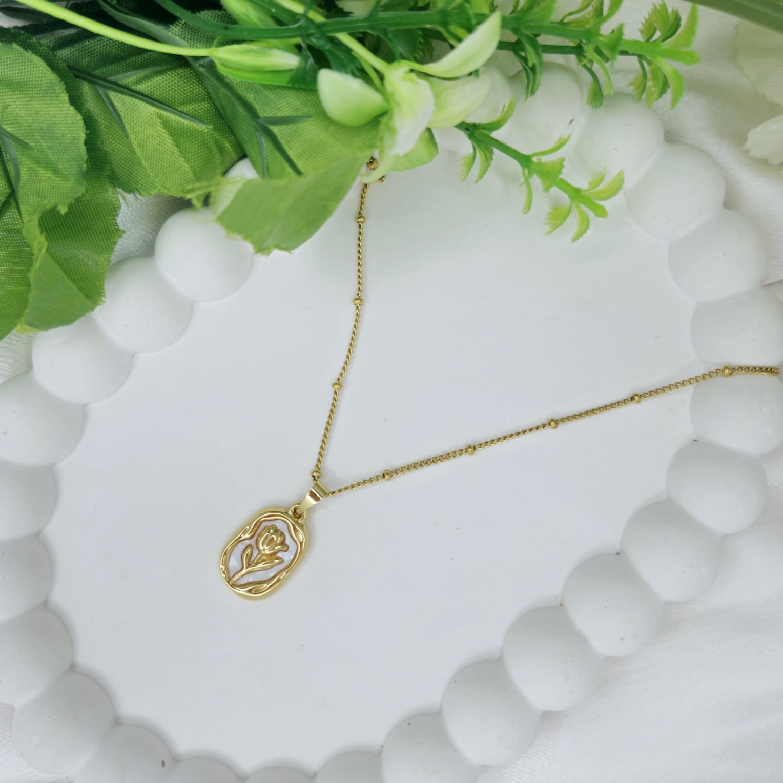 Gold necklace with a pendant on a white stone surface with green leaves.